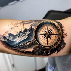 a man's arm with a compass tattoo on it and mountains in the background