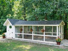 a white chicken coop sitting in the middle of a yard with potted plants on it