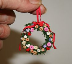 a hand holding a christmas wreath ornament with flowers and hearts on the front