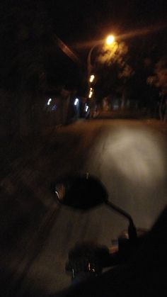 a person riding a motorcycle down a street at night with the lights on and trees in the background