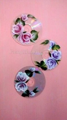 three cds with flowers painted on them sitting on a pink surface next to each other