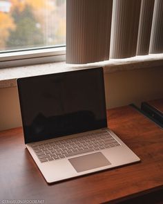 an open laptop computer sitting on top of a wooden desk next to a windowsill