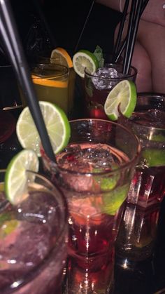 several glasses filled with different types of drinks and garnished with limes on the rim