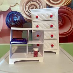 a white dresser with red knobs and drawers next to a colorful wallpapered background