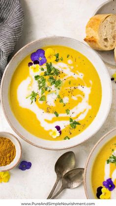 two bowls of soup with bread and purple pansies on the side next to it