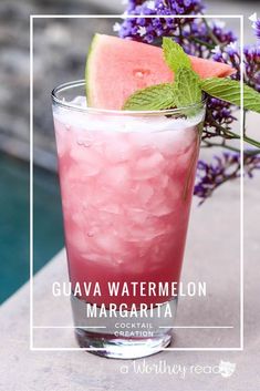 a watermelon margarita with ice and mint garnish in a glass next to purple flowers