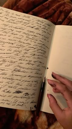 a woman's hand is holding an open book with writing on it and a pen