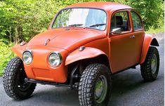 an orange car parked on the side of a road next to some grass and trees