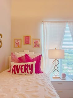 a bed with pink and white pillows on top of it next to a window in a bedroom