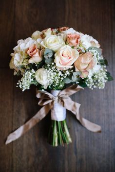 a bouquet of roses and baby's breath is tied to a white vase on a wooden table