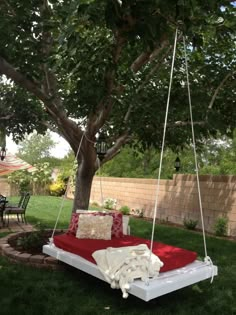 a bed that is in the grass with a red blanket on it, and an empty swing