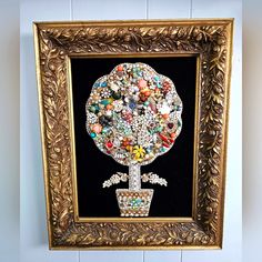 a gold framed artwork with beads and jewels on it's center piece is hanging on the wall