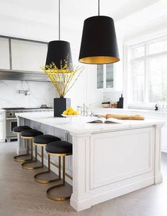 a kitchen island with four stools in front of it and a black lamp hanging from the ceiling