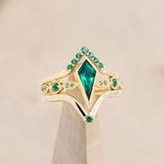 a gold ring with an emerald colored stone surrounded by smaller green stones on top of it