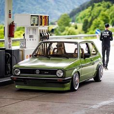 a small green car parked at a gas station next to a man walking by it