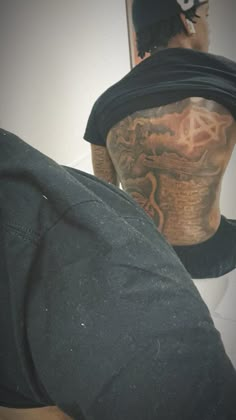 the back of a man's head with tattoos on it and his hat in front of him