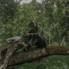 a man sitting on top of a tree branch in the forest with headphones on