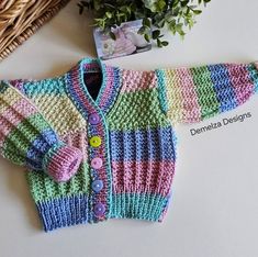 a knitted baby sweater next to a basket with flowers and a photo on it