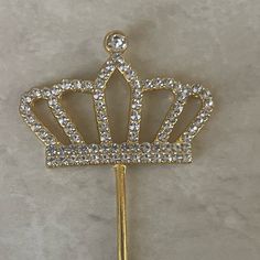 a gold crown brooch with crystal stones on it's back and a long handle