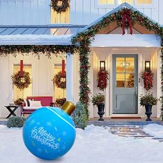 a large blue christmas ornament in front of a house with wreaths on it