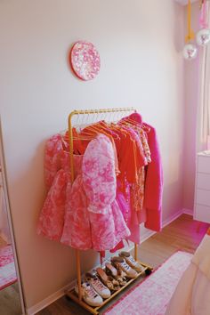 a rack with clothes and shoes on it in front of a pink wall, next to a bed