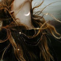 a woman's head with long hair blowing in the wind and sparkling lights behind her