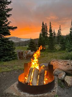 a fire pit in the middle of a field with trees and rocks around it at sunset