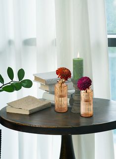 two vases with flowers are sitting on a table next to books and a candle