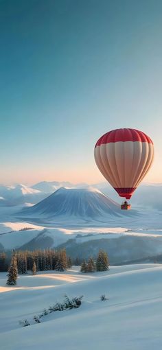 a hot air balloon in the sky over snow covered hills and trees with mountains in the background