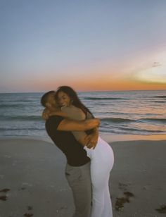 a man and woman hug on the beach at sunset