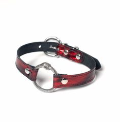 Classic o-ring collar is elevated with an intricate ouroboros snake o-ring and gorgeous black and red patent leather. This leather has a subtle metallic glimmer and is truly special. Fully lined in soft black suede and stitched for strength. Fit is adjustable with buckle. Maybe inspired by House of the Dragon. But dragons are pretty cool Collar is 3/4" wide, with a 1.25" o-ring. SMALL/MEDIUM (11-13")MEDIUM/LARGE (13-15")LARGE/X-LARGE (15-17") Custom sizing available. All pieces are MADE TO ORDER Snake Inspired Fashion, Dragon Choker, Skull Collar, Ouroboros Snake, Red Choker, O Ring Choker, Fantasy Necklace, Seattle Fashion, Jewelry Wardrobe