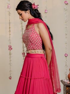 A three-piece fuchsia pink mirror lehenga set from the Redpine Designs collection. This pretty fuchsia pink mirror crop top blouse is paired with a pleated pink lehenga. The fuchsia pink color with mirror, poth, cutdana, shell, kasab work enhances the graceful georgette lehenga set. The fuchsia pink lehenga has beautiful pleats, layers, and frills with flare style. The fuchsia pink blouse features shell tassels, heavy mirror embroidery and a scoop neckline. The outfit is completed with a pink ne Georgette Choli With Mirror Work, Pink Sleeveless Lehenga For Eid, Sleeveless Pink Lehenga For Eid, Pink Georgette Sets With Cutdana, Red Cutdana Party Wear Sets, Pink Palazzo Set With Mirror Work For Reception, Pink Sleeveless Party Wear Sets, Anarkali Chinon Choli, Anarkali Style Chinon Choli