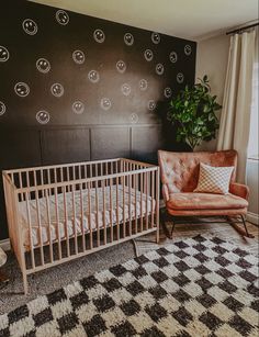 a baby's room with a crib, chair and potted plant