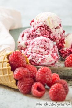 three scoops of ice cream and raspberries on a plate next to some waffle cones