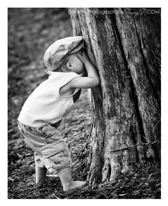 a little boy standing next to a tree in the forest with his head on it's trunk