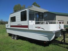 a white boat sitting on top of a grass covered field next to a trailer and building