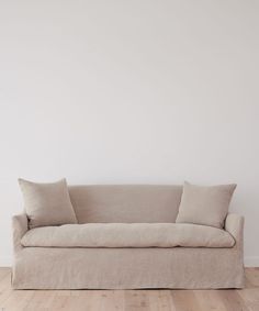 a couch sitting on top of a hard wood floor next to a white wall with two pillows