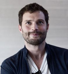 a man with a beard wearing a black jacket and white shirt smiling at the camera