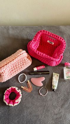 the contents of a pink crocheted purse are laid out on a gray blanket