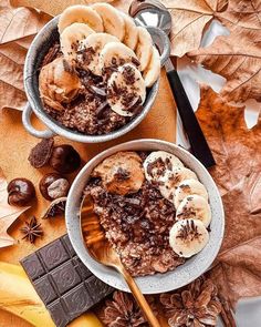 two bowls filled with food sitting on top of a table next to leaves and spoons