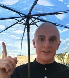 a bald man holding an umbrella with his finger up in front of him and making the peace sign