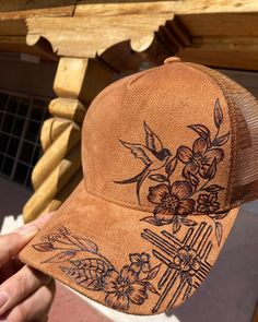 a person holding up a brown trucker hat with flowers and crosses drawn on it