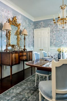 an elegant dining room with blue and gold wallpaper, chandelier, and wooden table