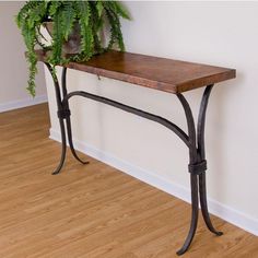 a wooden table sitting on top of a hard wood floor next to a potted plant