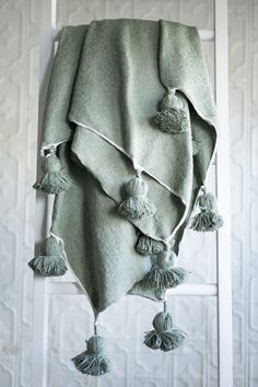 a blanket with tassels hanging on a ladder in front of a white wall