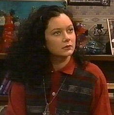 a woman with long black hair standing in front of a book shelf and looking off to the side