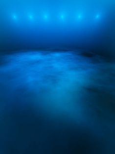 an empty blue room with lights shining in the dark water and fog on the floor