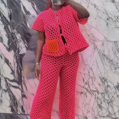 a woman in pink crocheted clothing standing next to a marble wall and talking on a cell phone