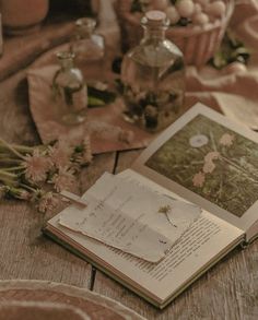 an open book sitting on top of a wooden table next to flowers and vases