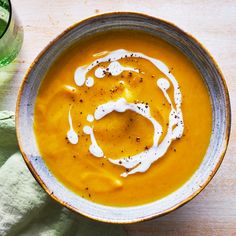 there is a bowl of soup with cream on the table next to a glass of water